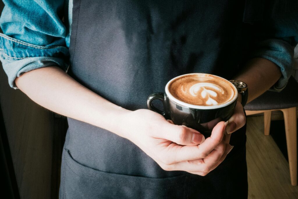 A barista holds a coffee cup with beautiful latte art in a cozy café setting.